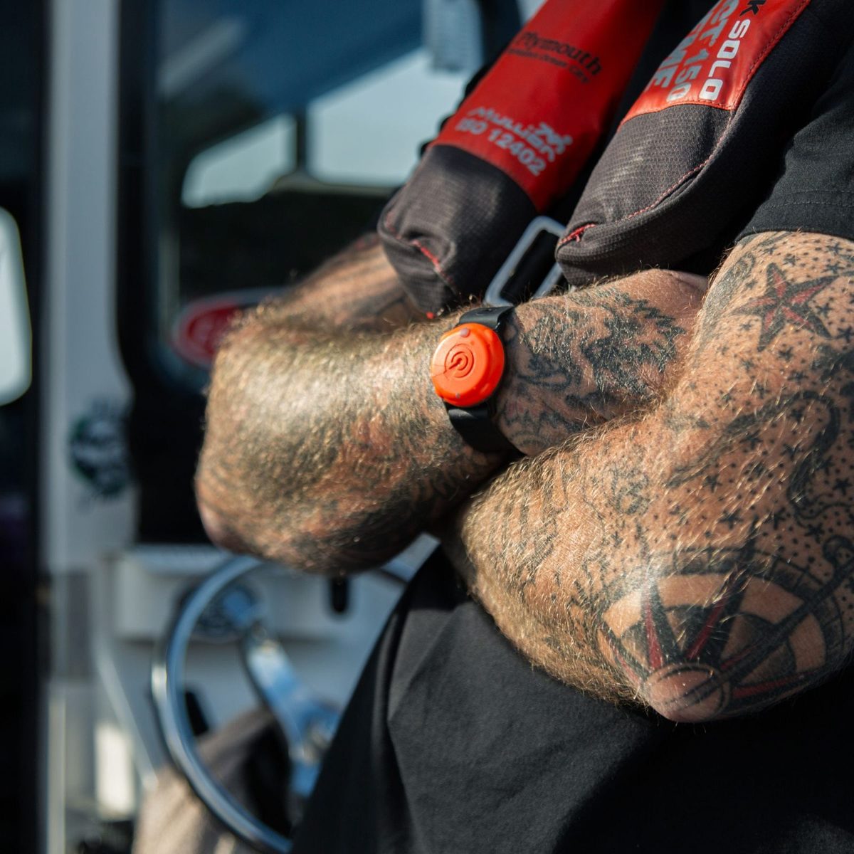 Skipper in a lifejacket wearing an orange OLAS Tag on his wrist at the wheelhouse door